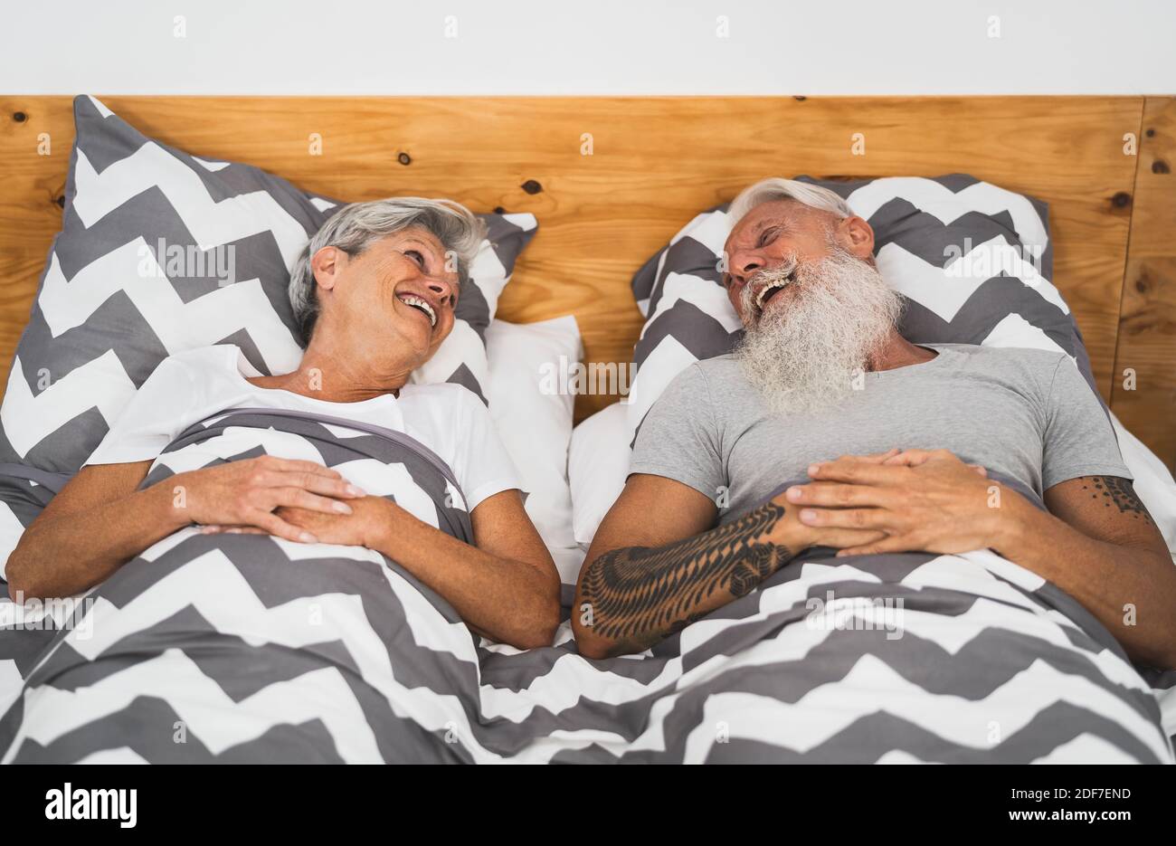 Happy senior couple smiling together in bed - Hipster mature people having funny bed time - Elderly lifestyle and love relationship concept Stock Photo