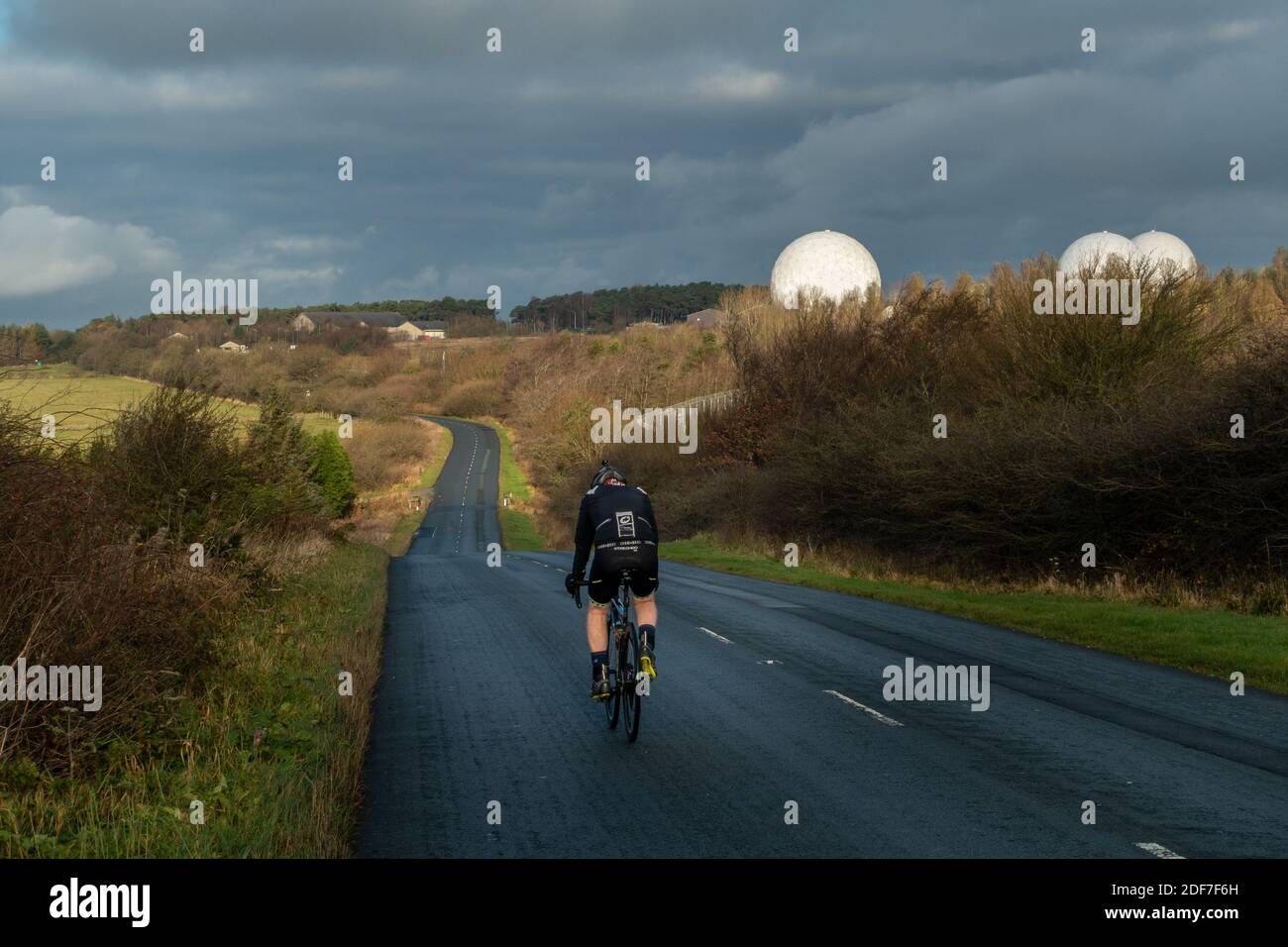 Cyclist cycling the B6461 past RAF Menwith Hill with white circular radomes of satellite ground station visible, North Yorkshire, England, UK Stock Photo