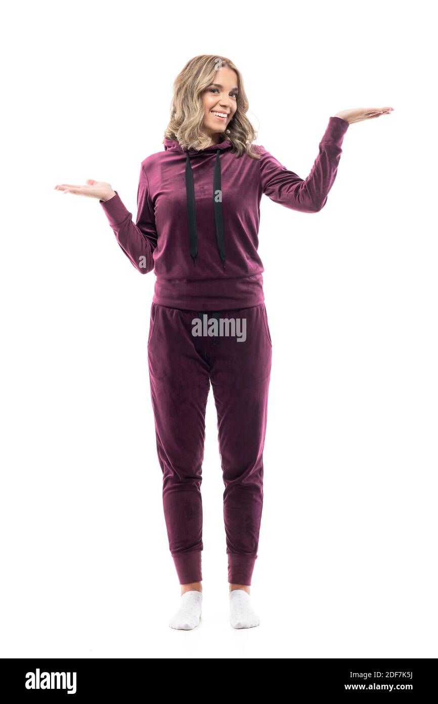 Happy pretty girl in leisurewear sweatsuit having dilemma weighting or choosing with raised hands. Full body length isolated on white background. Stock Photo