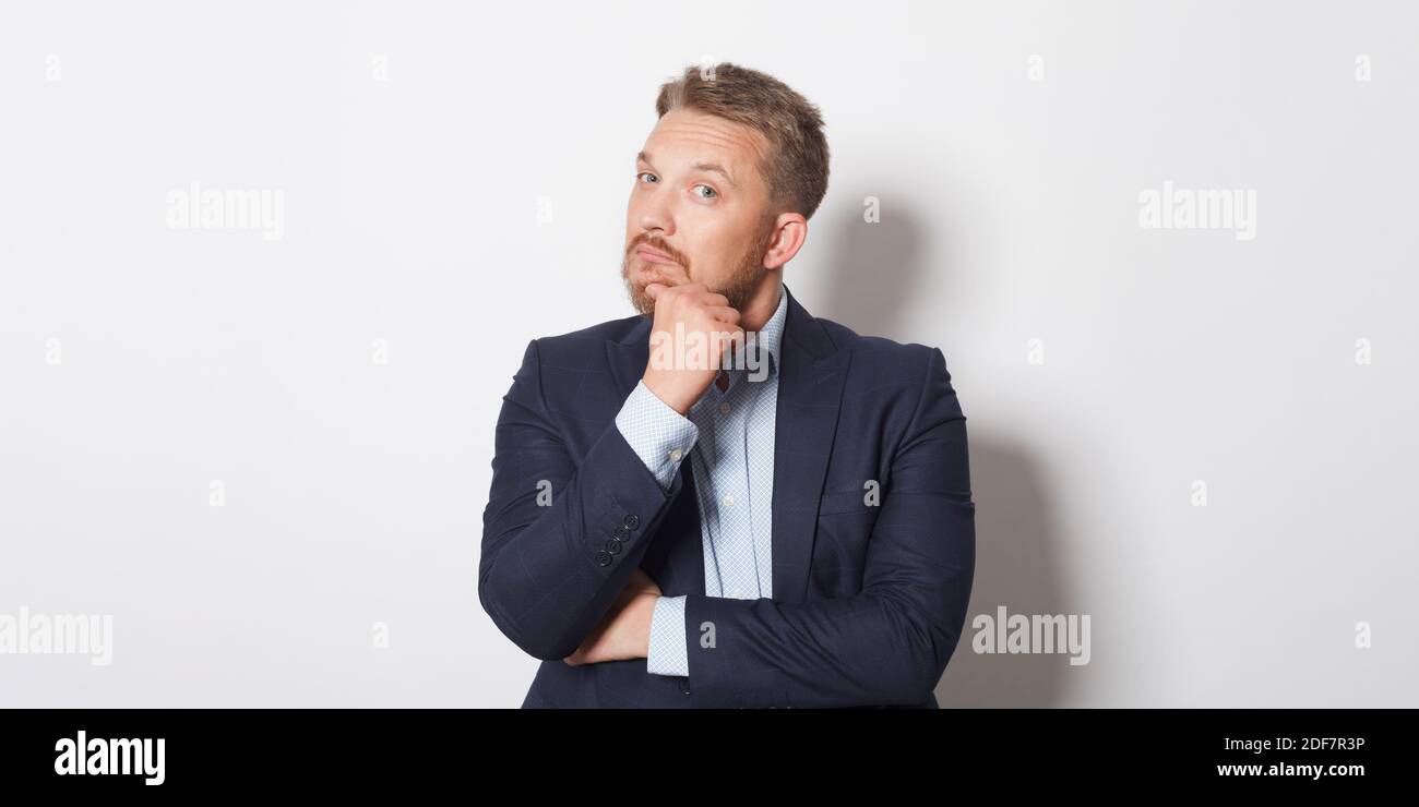 Man looking thoughtfully and rubbing his chin while standing against white background. Stock Photo