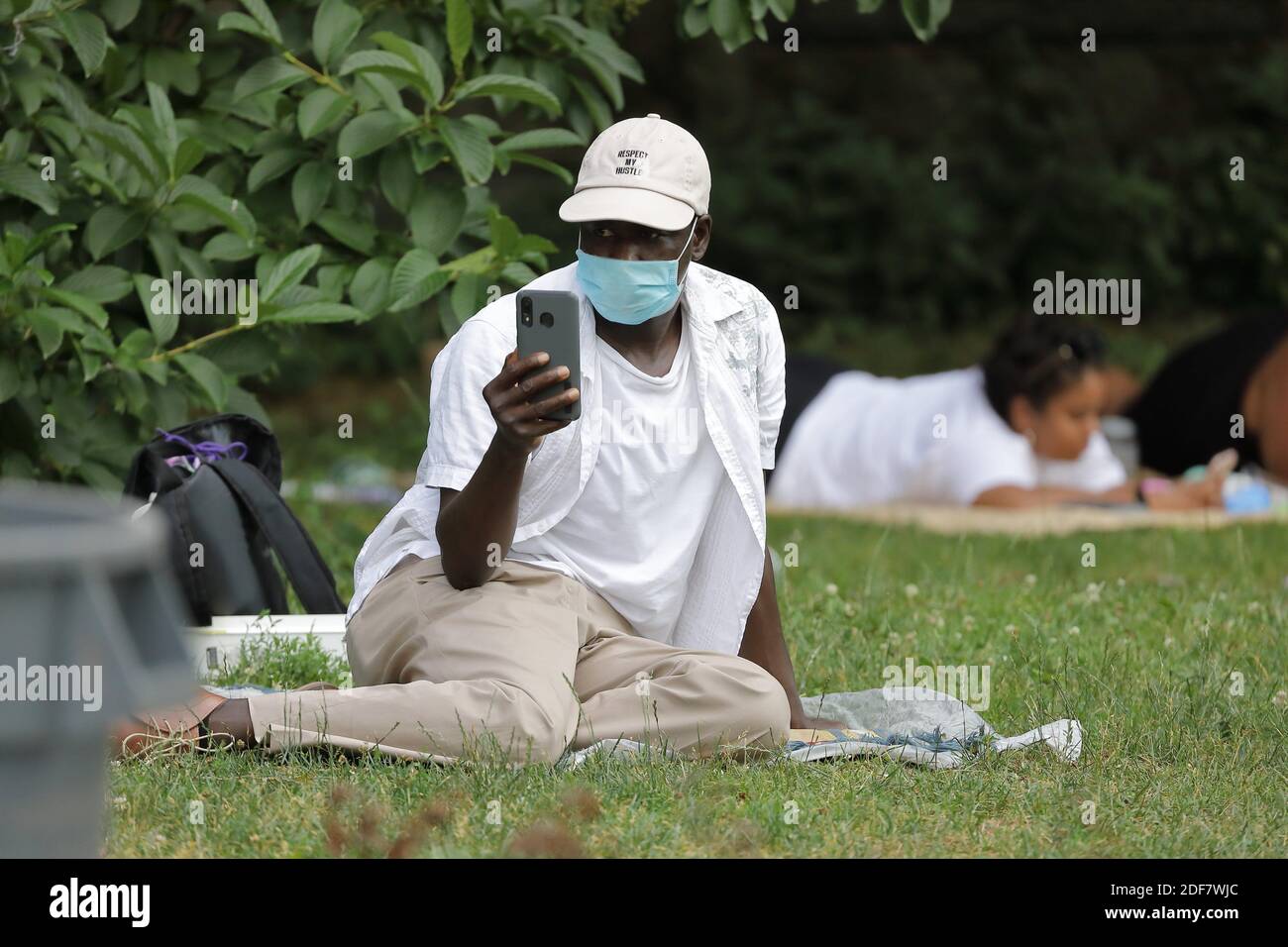 Black man looking at the phone sitting on the grass of a park during the coronavirus COVID19 pandemic Stock Photo
