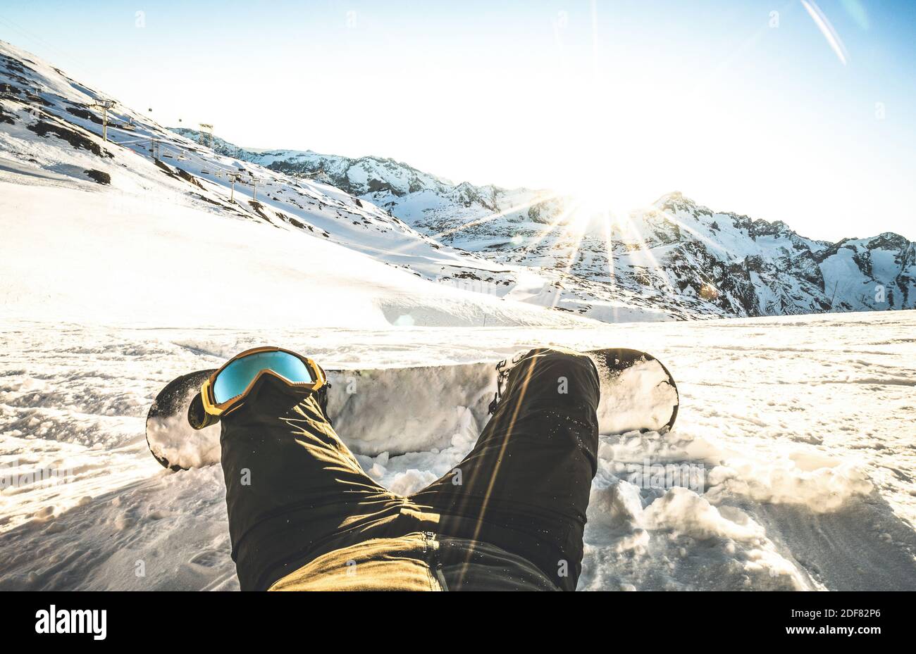 Snowboarder sitting at sunset on relax moment in european alps ski resort - Winter sport concept with guy and snowboard on mountain top ready to ride Stock Photo