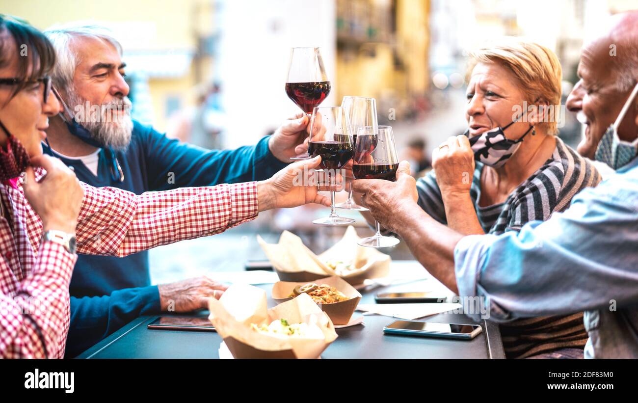 Senior couples toasting red wine at restaurant bar with face masks - New normal lifestyle concept with happy people having fun together at bar outdoor Stock Photo