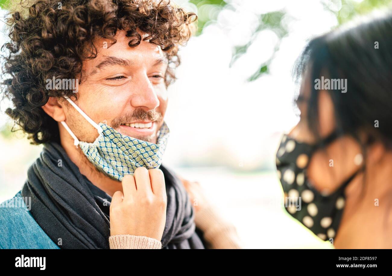 Happy couple of lovers looking at each other with open face mask - Love and hope concept at covid time with guy and girl on tender relationship moment Stock Photo