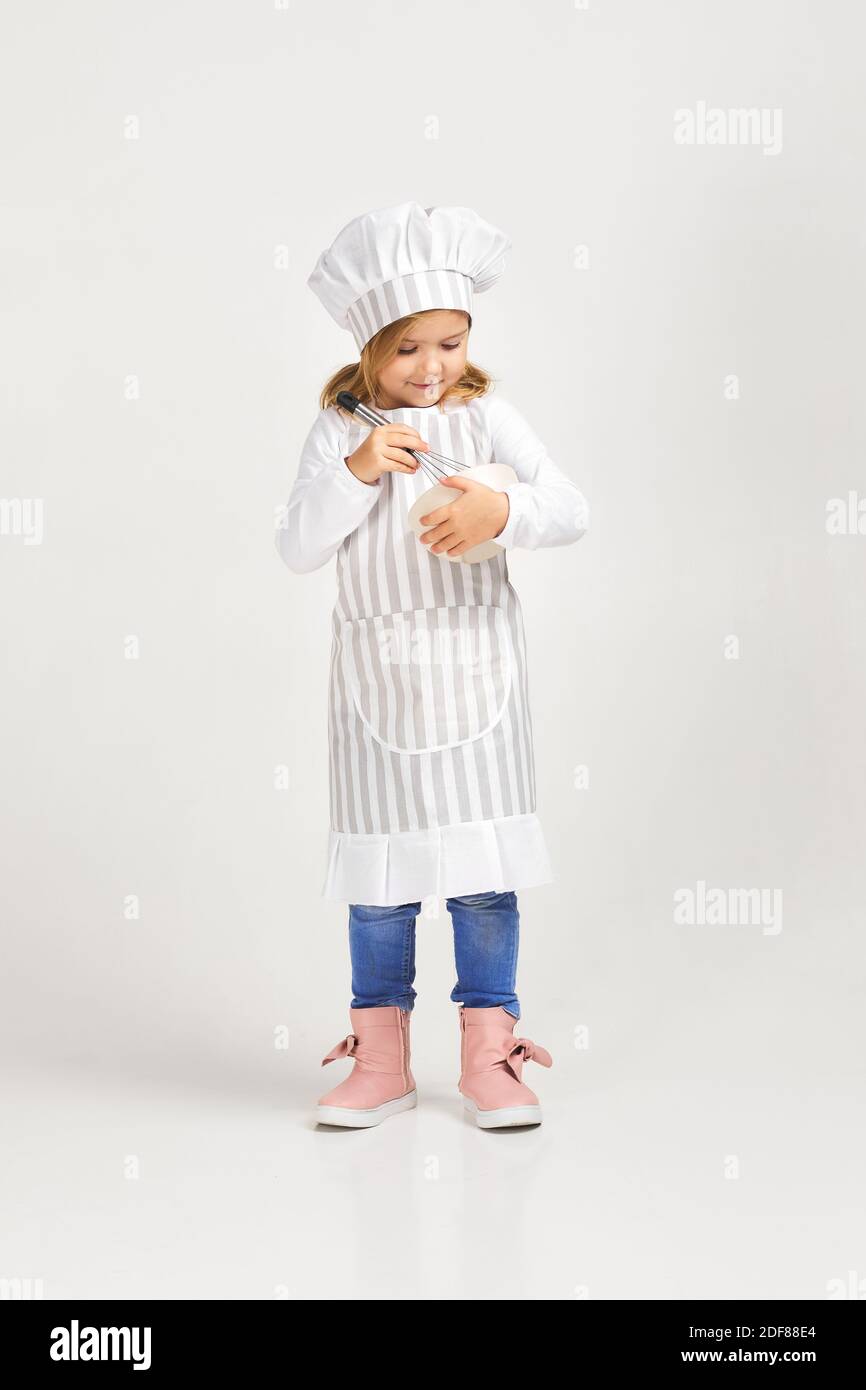 adorable little girl in cooker uniform with bowl and whisk. child