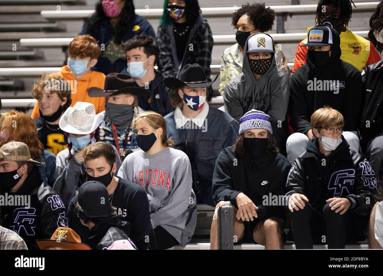 Chilly Cedar Ridge students wear masks and huddle in the stands at a high school football game at Dragon Stadium in Round Rock, Texas on a cold and windy Friday night during the COVID pandemic. Students did not socially distance themselves. Stock Photo