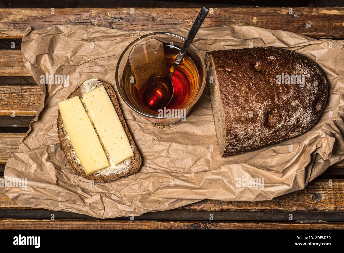 Brown bread sandwich with cheese and butter, a cup of black tea, half a loaf of brown bread on paper bag. Stock Photo