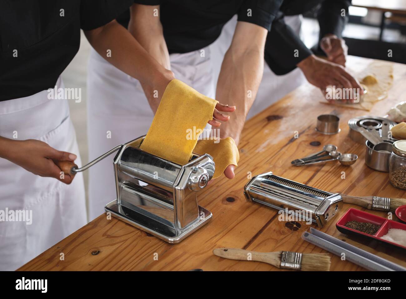 Mid section of male and female chef processing pasta sheet in machine at restaurant kitchen Stock Photo