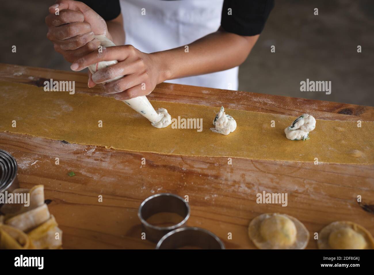 Mid section of chef adding fillings over ravioli pasta sheet at restaurant kitchen Stock Photo