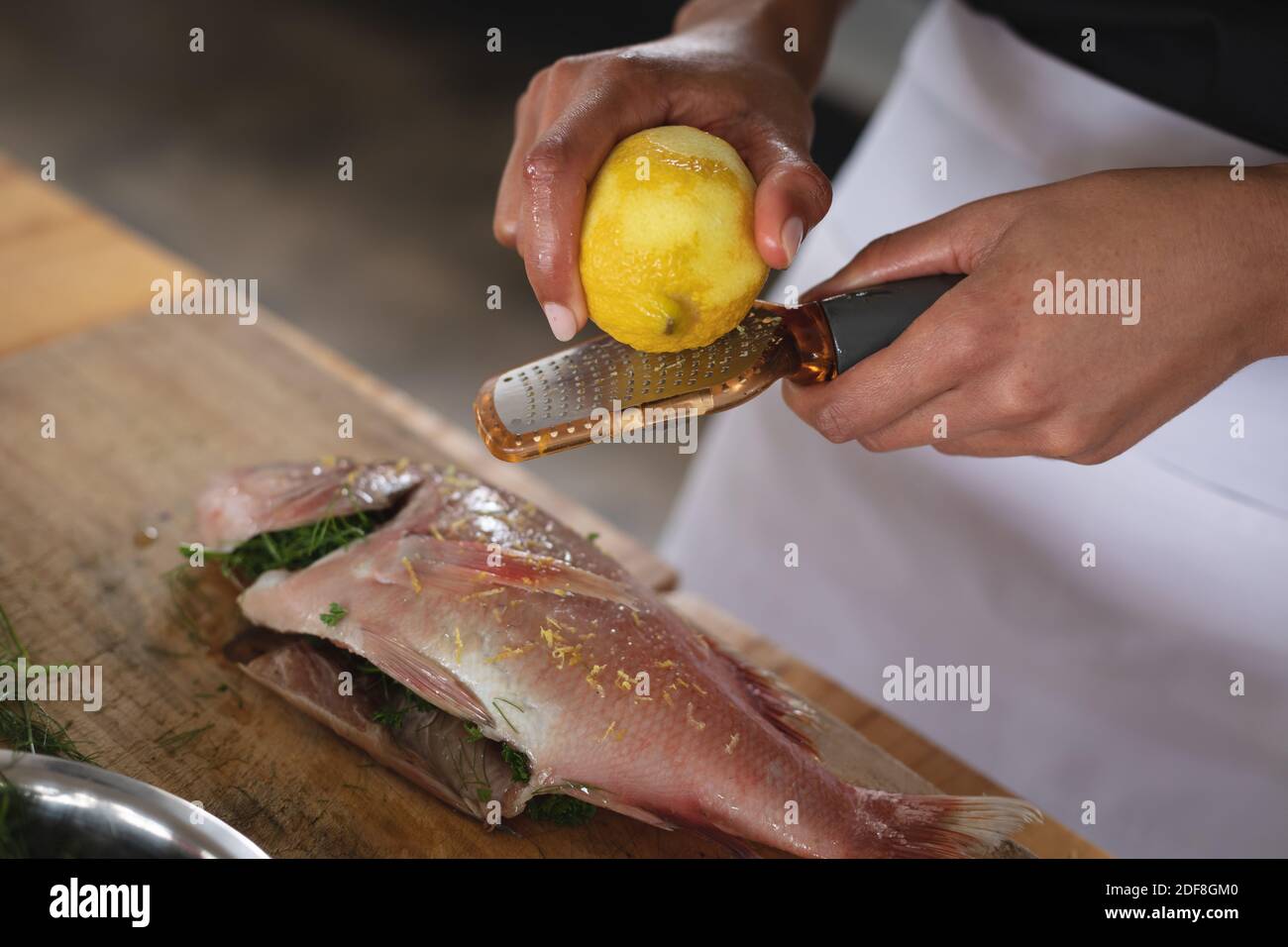 Mid section of chef grating lemon rind on roasted fish in restaurant kitchen Stock Photo