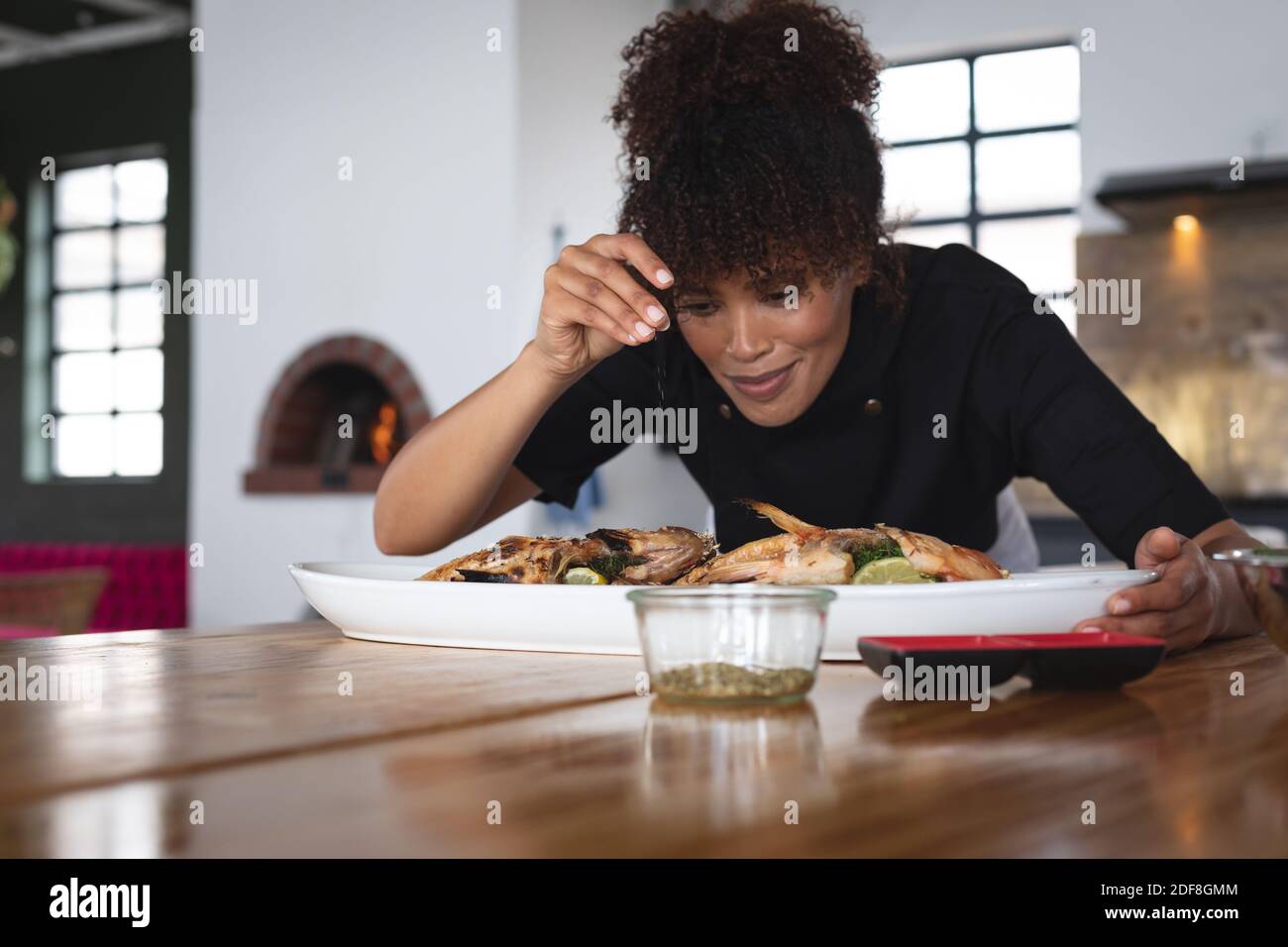 Female african american chef adding salt over roasted fish in food