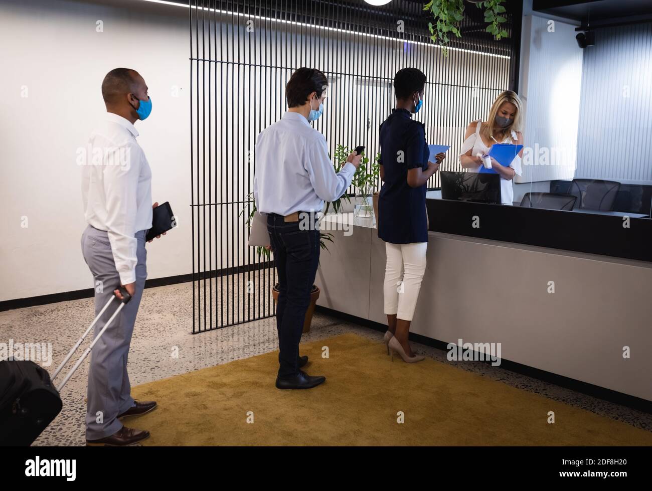 Reception Group Diverse group wearing masks queing to reception, receptionist holding ...