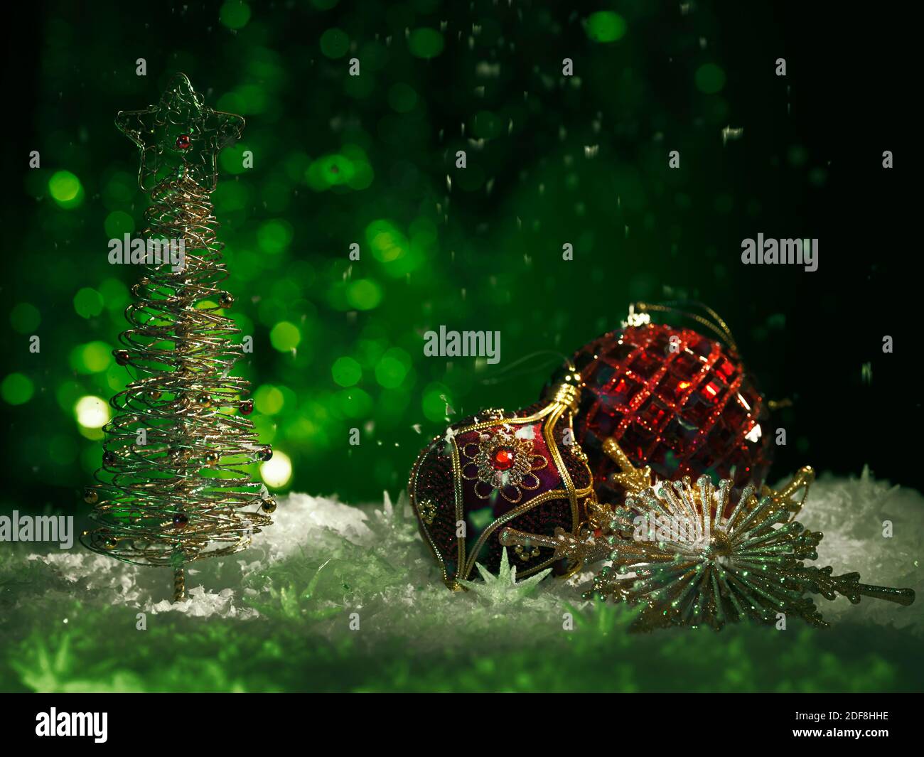 Red Christmas ornament and a shiny Christmas tree on green background with falling snow in moody dark settings. Artistic winter holidays, new year con Stock Photo