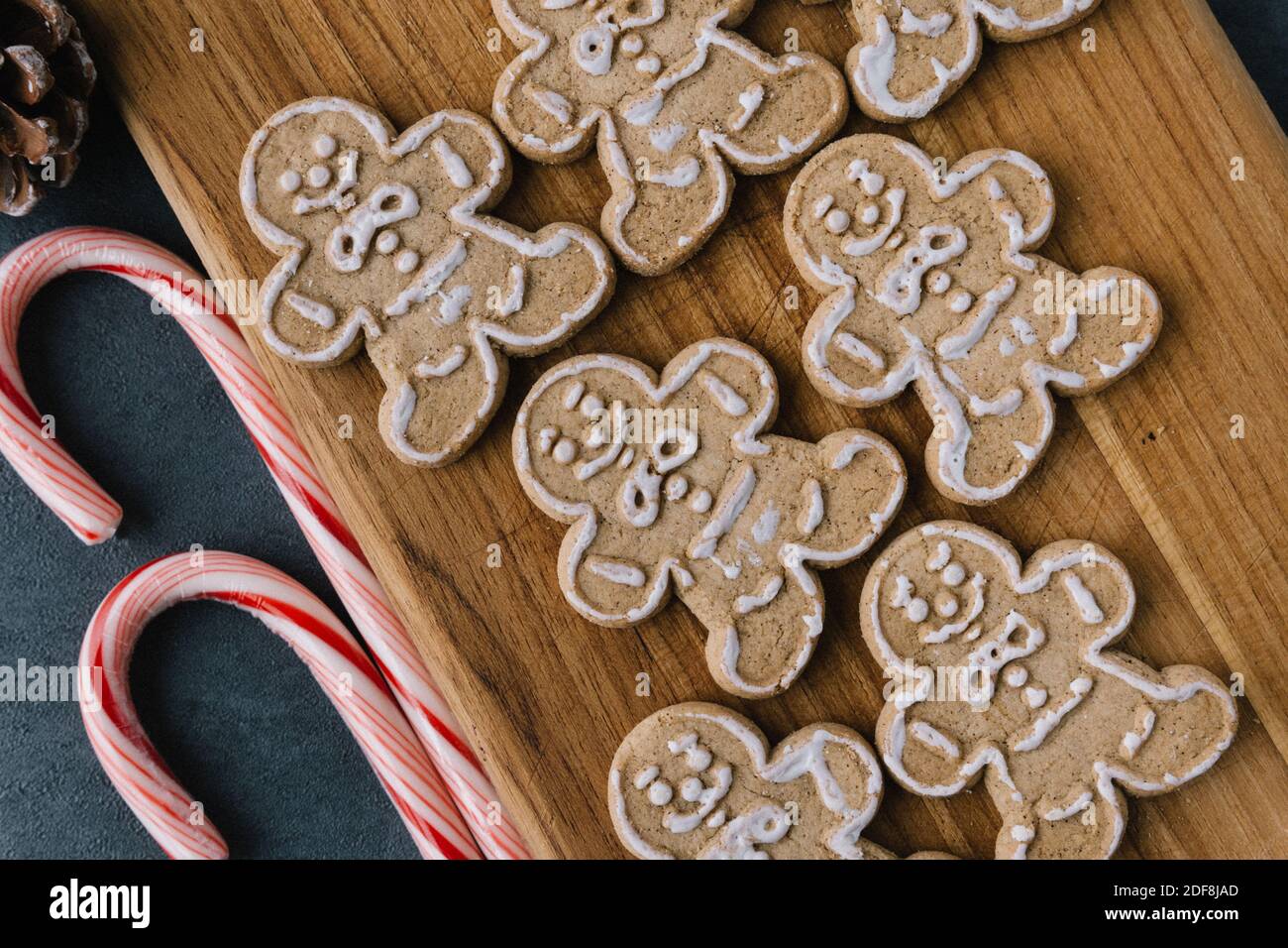 Christmas Gingerbread Man Cookies on Wooden Board With Ribbons, Pine Cones, Bells, and Ornaments, On Dark Slate Texture Stock Photo
