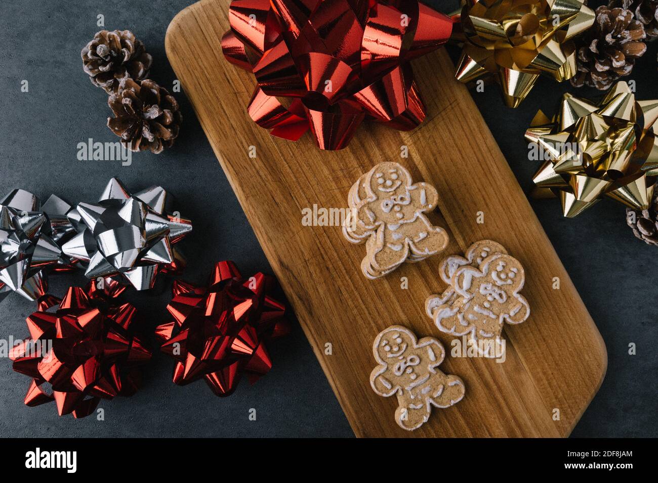 Christmas Gingerbread Man Cookies on Wooden Board With Ribbons And Pine Cones On Dark Slate Texture Stock Photo