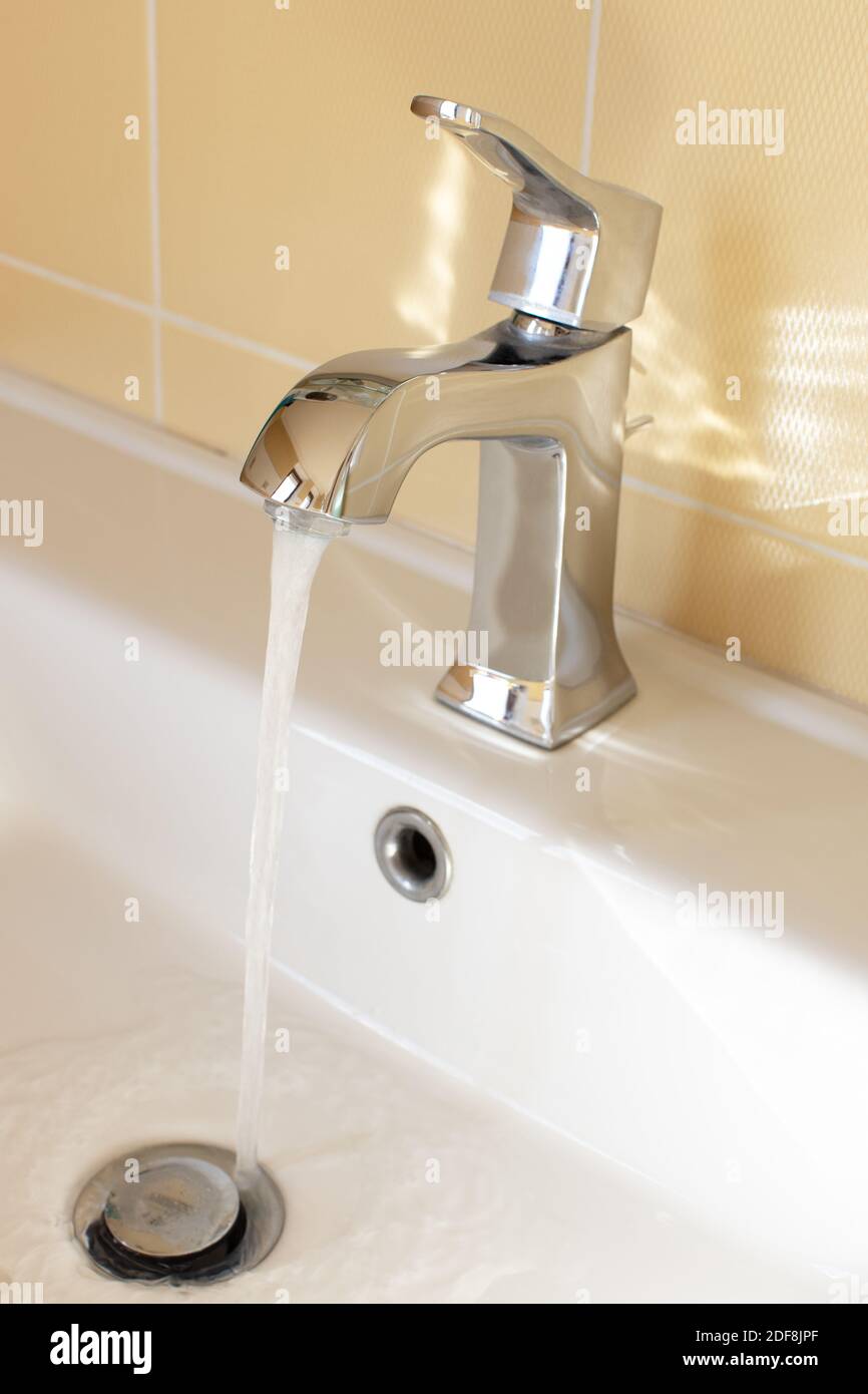 Modern faucet in yellow bathroom with running water, close up, side ...