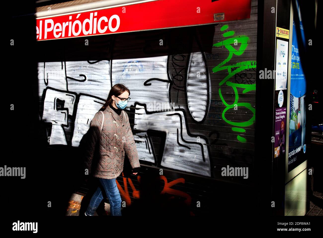 Woman wearing mask walking past a closed kiosk, Barcelona, Spain. Stock Photo