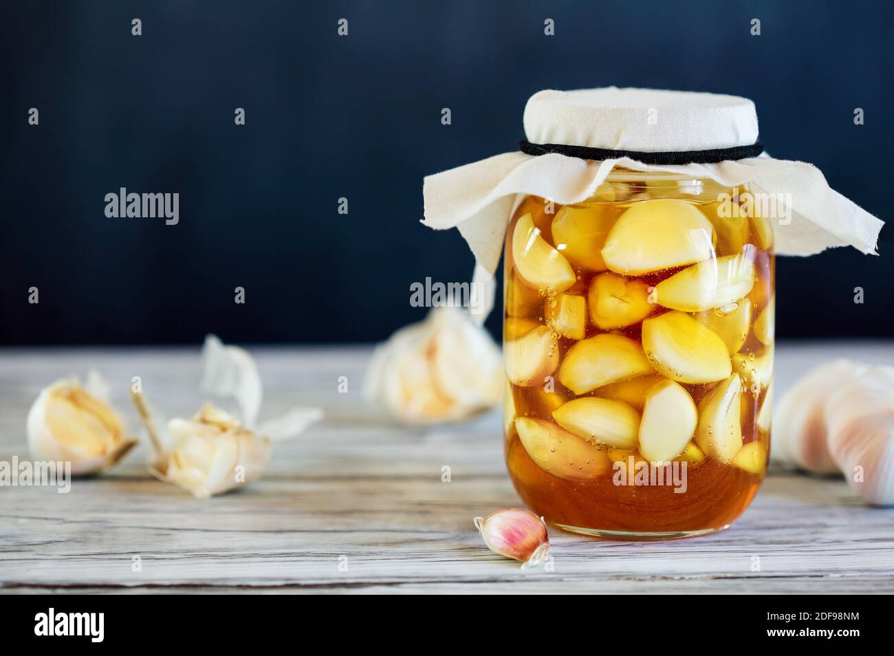 Fermented garlic cloves in a jar of honey, a rich source of probiotics, over a rustic wood background table. Selective focus with blurred background a Stock Photo