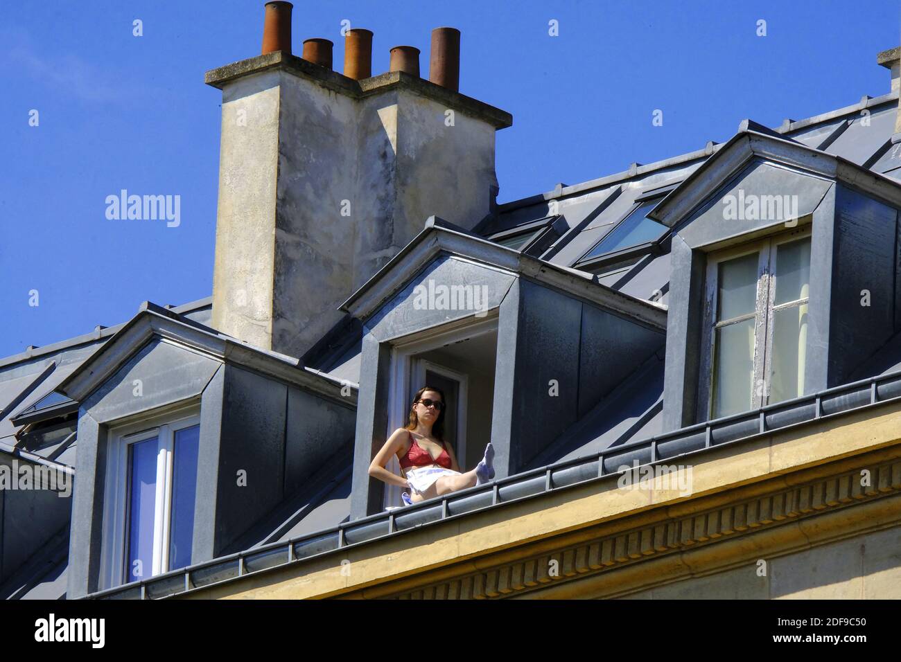 A confined Parisian enjoy sunny spring weather on the window during lockdown imposed to slow the spreading of the coronavirus disease (COVID-19) in Paris. after the announcement by French President Emmanuel Macron of the strict home confinement rules of the French due to an outbreak of coronavirus pandemic (COVID-19) on March 18, 2020 in Paris, France. the French will have to stay at home, France has closed down all schools, theatres, cinemas and a range of shops, with only those selling food and other essential items allowed to remain open. under penalty of sanctions, prohibiting all but esse Stock Photo