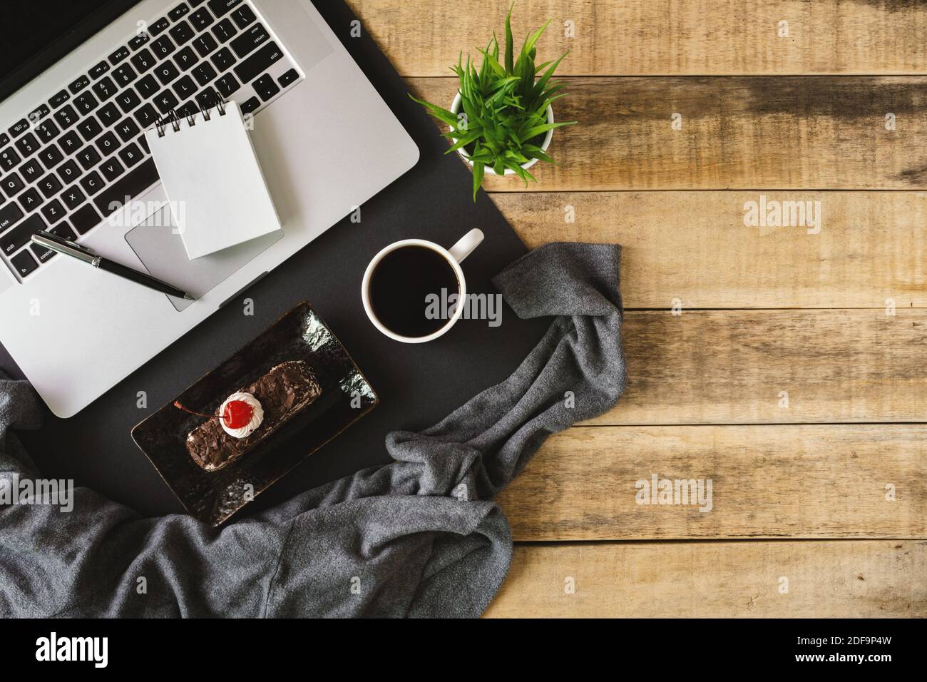 Laptop, small spiral notepad, butterscotch cake and cup of coffee on rustic wood. Flat lay. Stock Photo