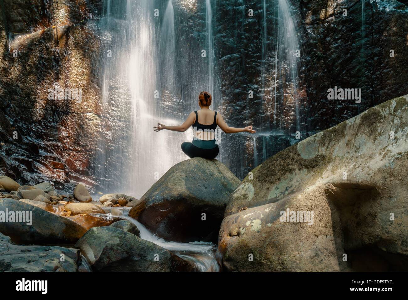 Woman doing yoga pose in front of a waterfall at Kionsom Park, Sabah ...