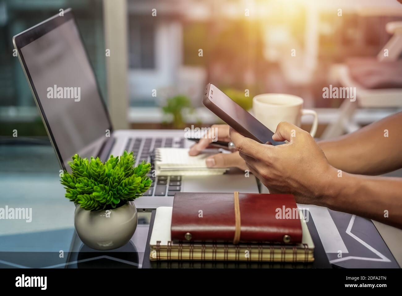 Holding a smart phone while working on laptop at home office. Freelance lifestyle. Stock Photo