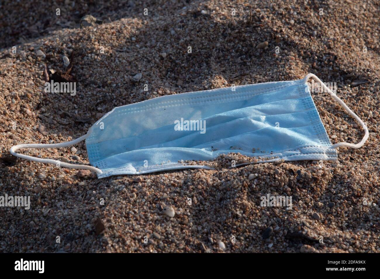 A protective face mask is seen discarded in the sand on a beach in