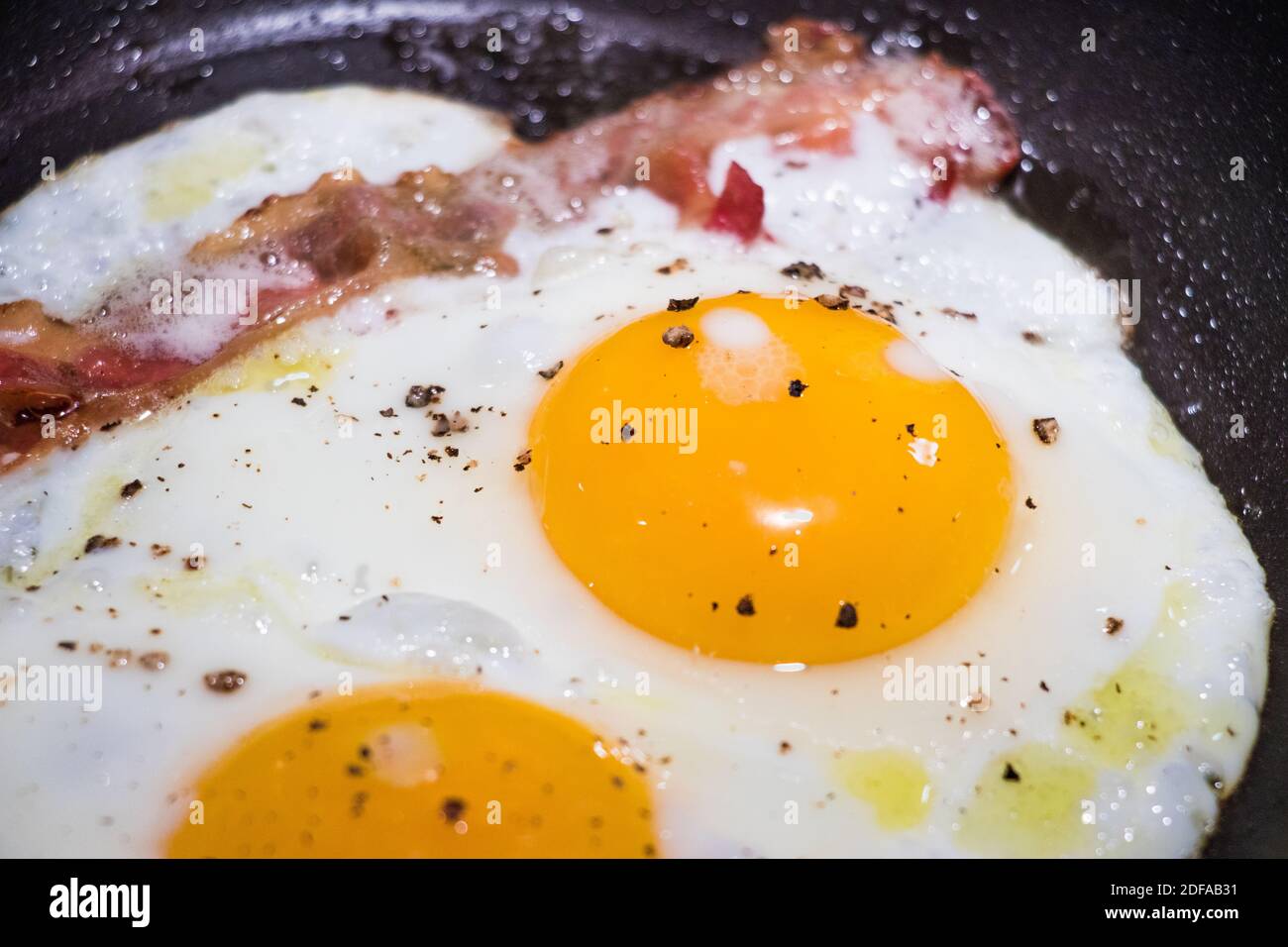 Cooking for breakfast sunny side up eggs and bacon in a fry pan Stock