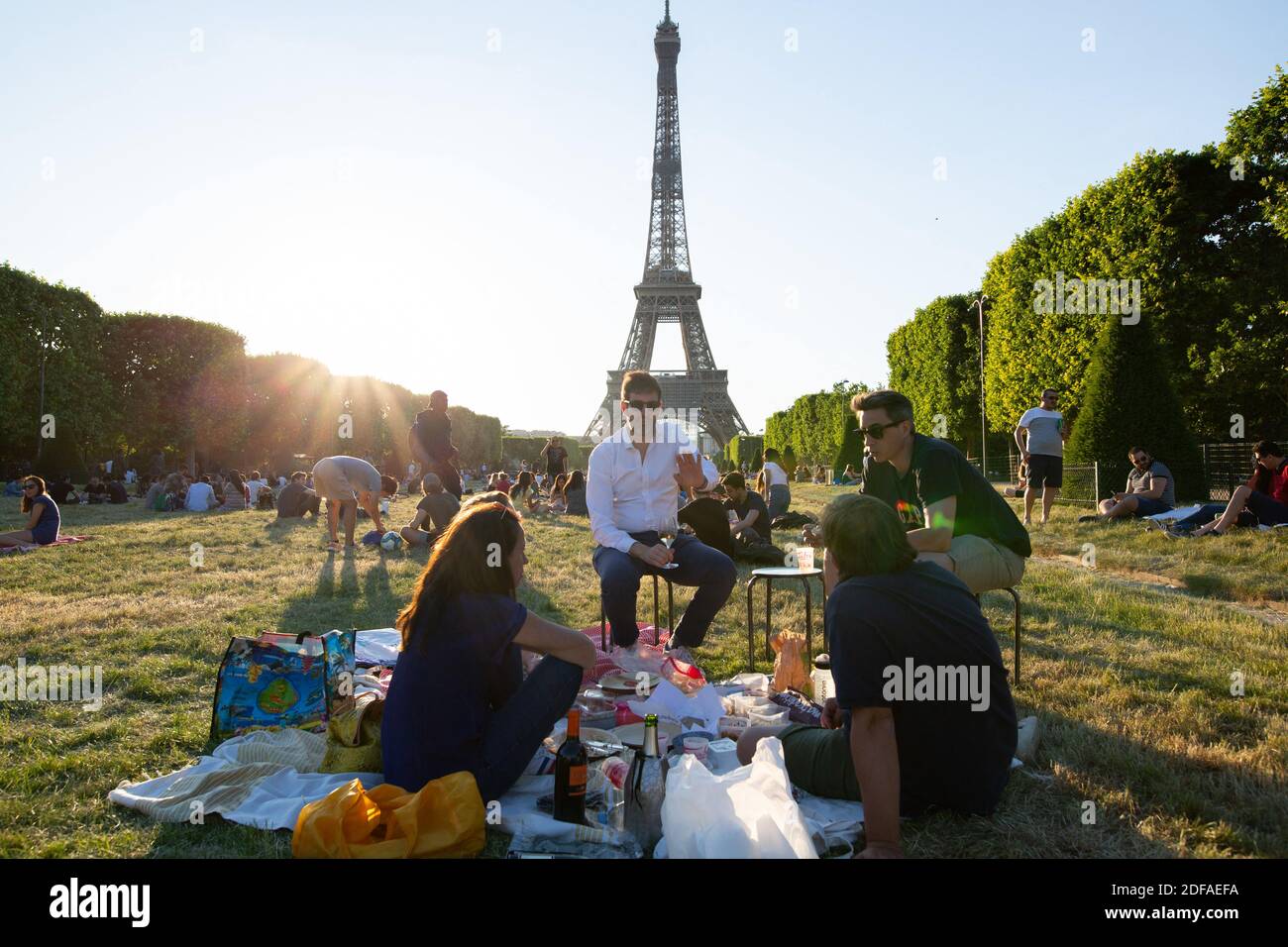 People sit and enjoy the sun and picnic and drink wine in wine glasses in  the champs de mars next to the eiffel tower in Paris on May 30, 2020, on the