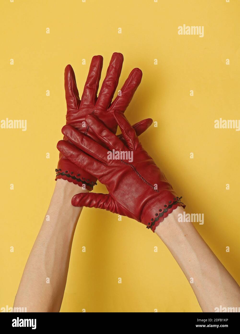 Skinny female hands wearing leather red gloves on yellow background