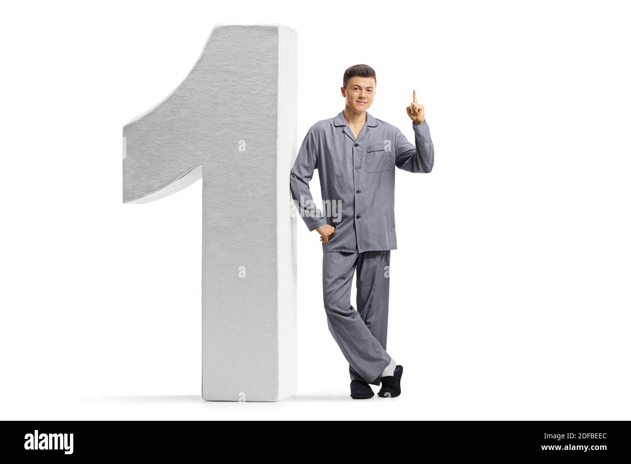 Full length portrait of a young man in pajamas leaning on a big number one and pointing up isolated on white background Stock Photo