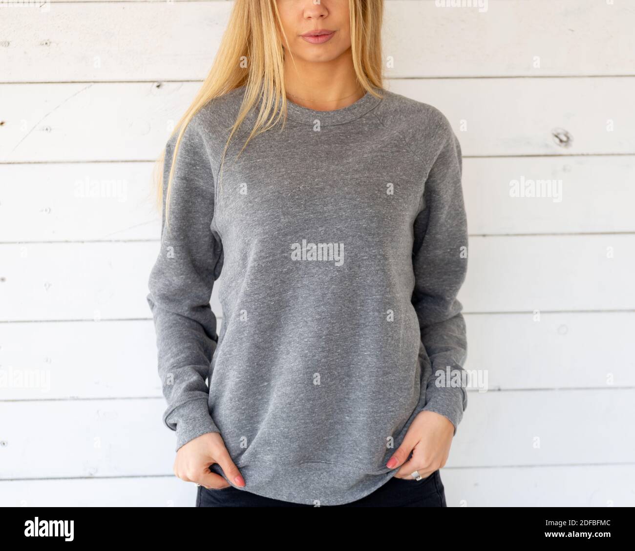 The fornt view of blond hair woman wearing a grey hoodie or blouse. She is standing on white board. Fashion outfit for mockup. Stock Photo