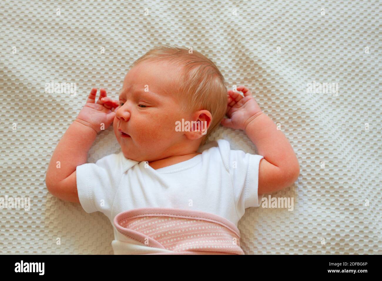 Cure newborn baby girl wearing white bodysuit lying on the bed Stock Photo