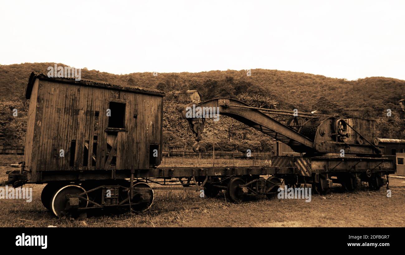 Old, rusty and abandoned waggon placed at a grass field with hills behind it [Sepia] Stock Photo