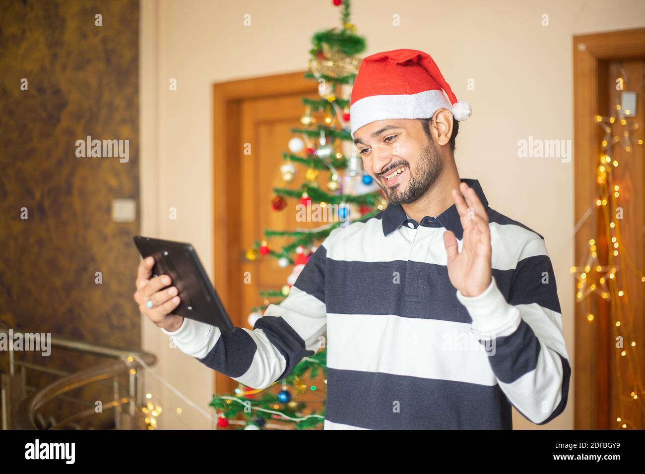 Young man celebrating christmas congratulating relatives over online video call on tablet at home, new year, holiday, party. Stock Photo