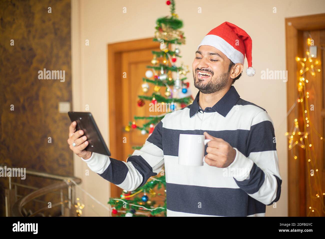 Christmas celebration, Cheerful Young man talking over video call conference on tablet at home holding coffee mug in hand, new year, holiday, party, w Stock Photo