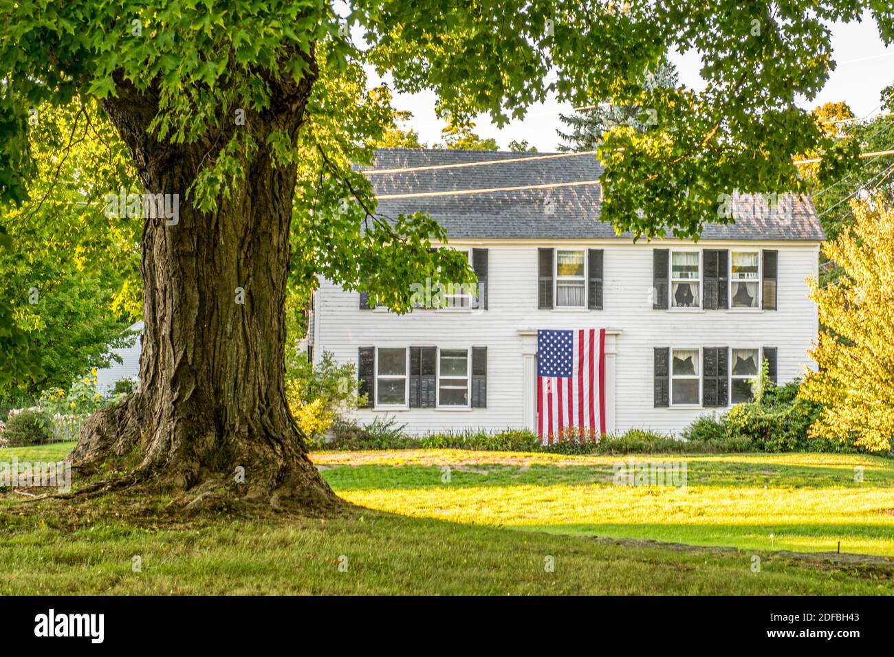 A large American Flag hangs over the front door of this colonial style home in Phillipston, Massachusetts Stock Photo