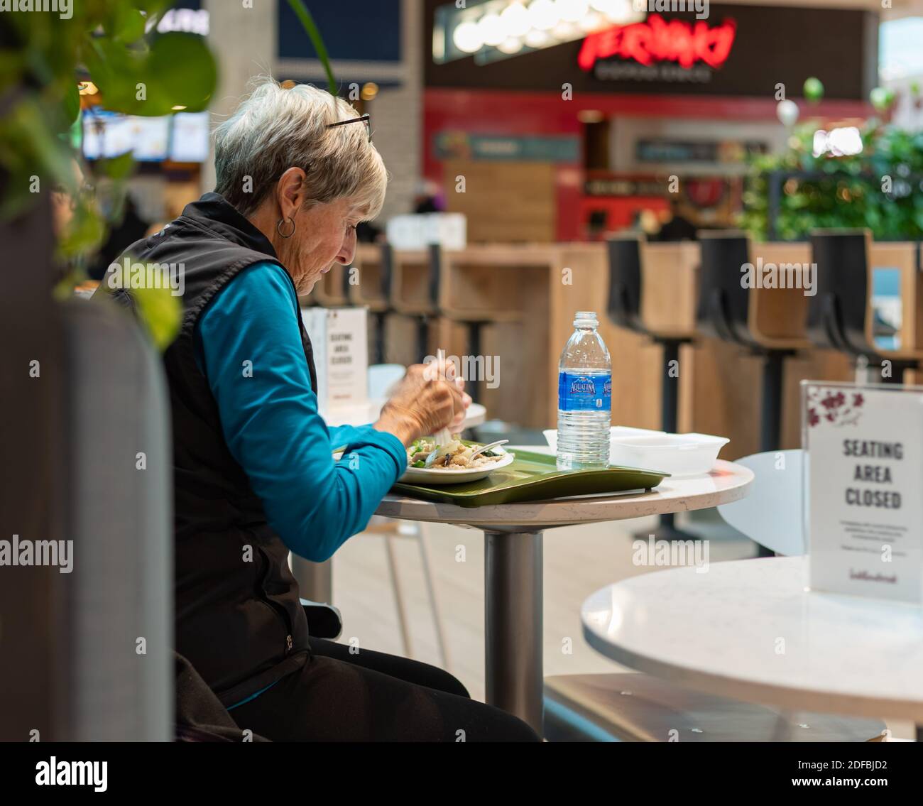 A senior woman sitting in the cafeteria and having hot lunch. Selective focus, street view. Langley, BC, Canada-November 9, 2020. Stock Photo