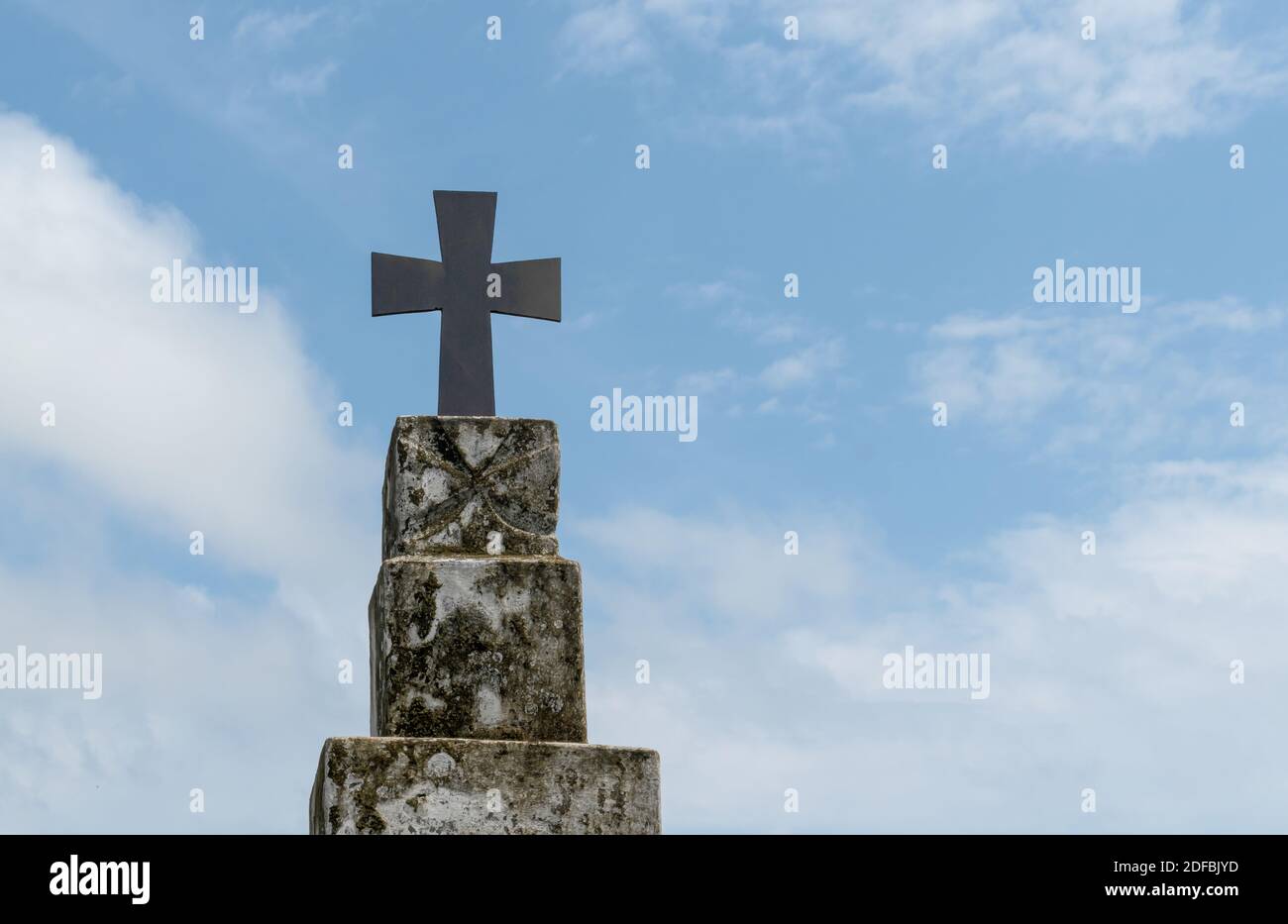 Beautiful photo of holy cross fixed on top of vintage pillar with blue sky and sparse white clouds in background. Stock Photo