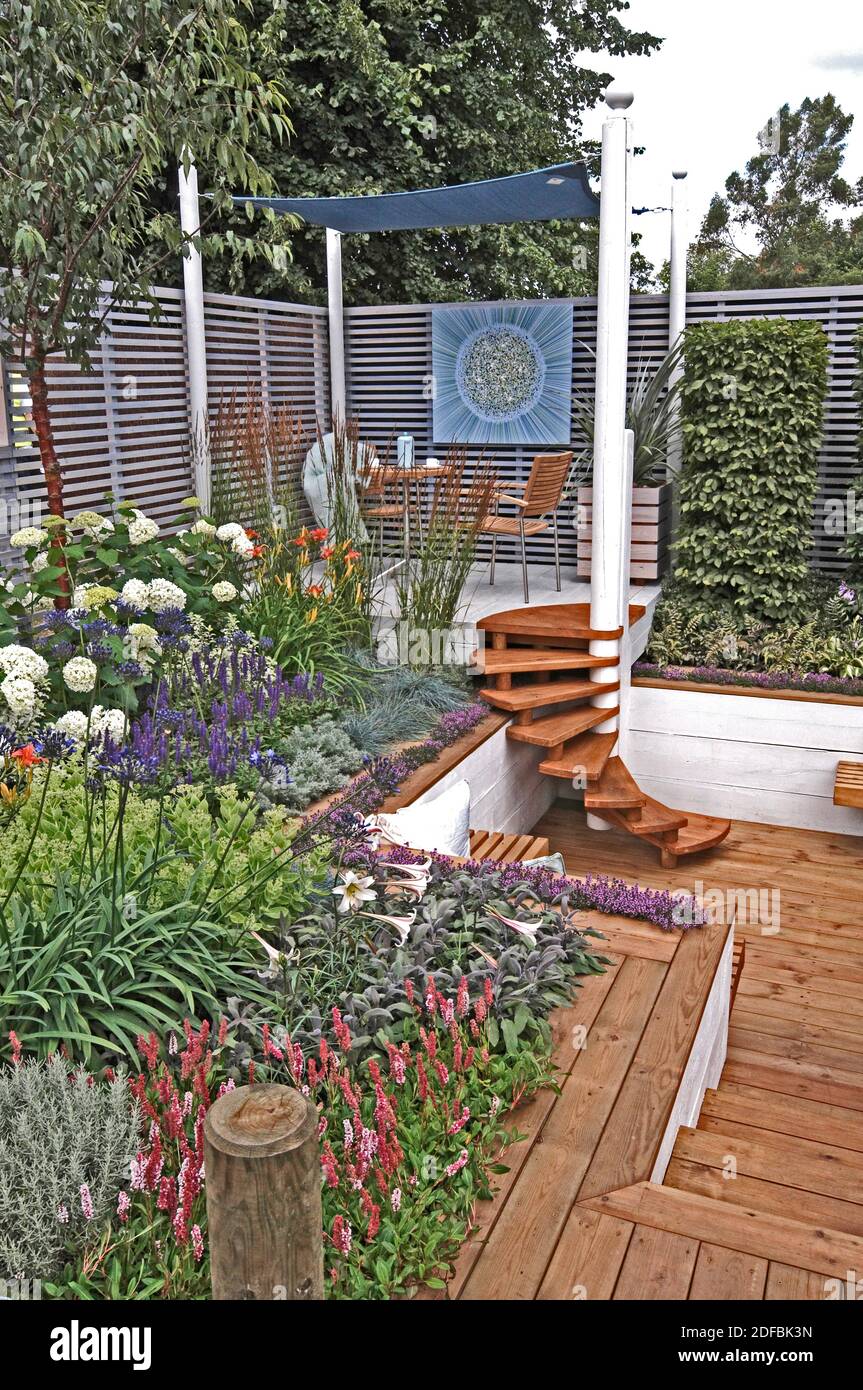 GARDEN WITH SEATING AND DECKING FOR AN URBAN GARDEN. Planting around the raised covered seating area with decking  with colouful mixed planting. Stock Photo