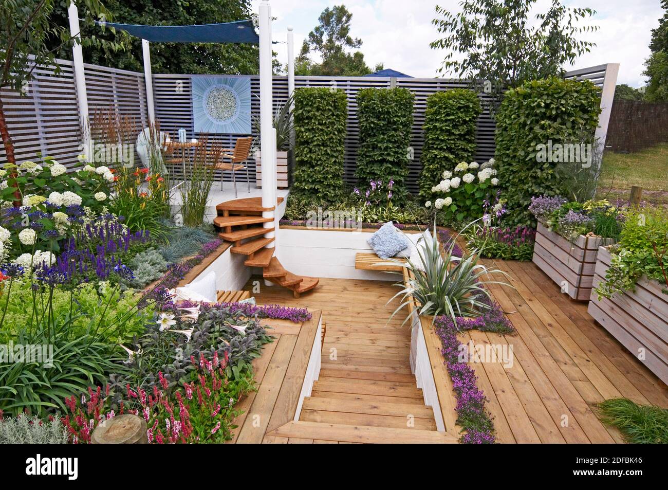A COLOURFUL SHOW GARDEN WITH SEATING AND DECKING FOR AN URBAN GARDEN. Planting around the raised covered seating area with decking  and a sunken area Stock Photo