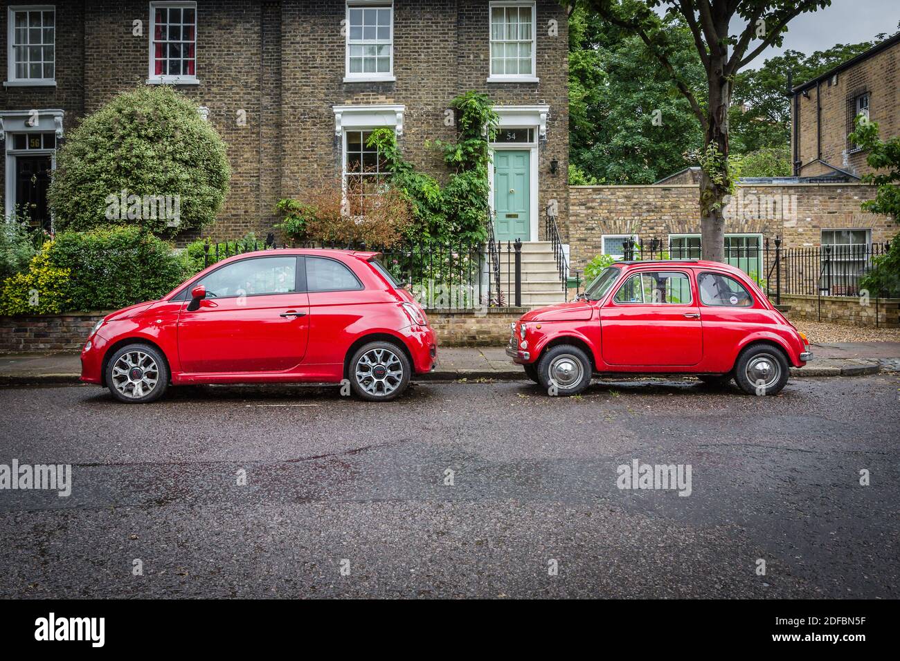 Two generations of the Fiat 500 in the same red colour parked down a leafy London street. Stock Photo