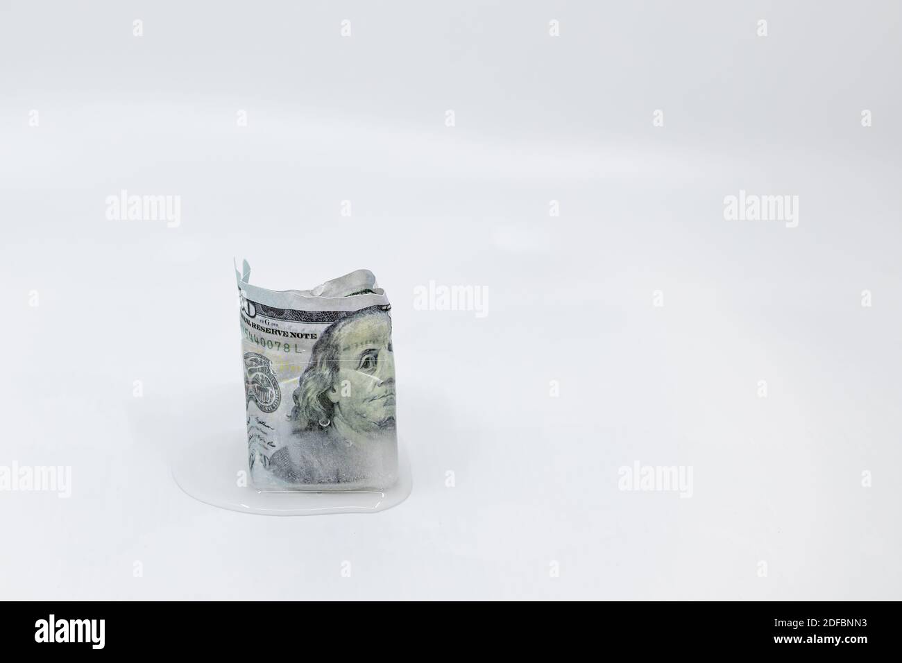 Slowly melting 100 dollar bill banknote frozen in an ice cube on white background with copy space. Concept of frozen assets, frozen economy, cold mone Stock Photo