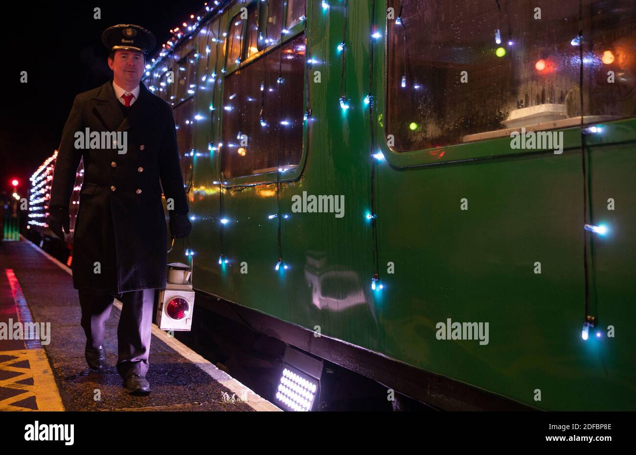 A guard carries a lamp past the world's first digital LED train, created using thousands of fully controllable colour mixing LED lights, whilst at Alton station during a preview of Steam Illuminations at Watercress Line, which opens to the public on Friday December 4. Stock Photo
