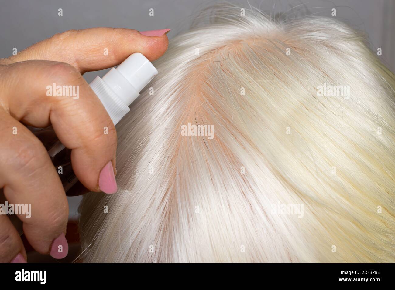 The woman puts on her hair a tonic of hydrolyte from a bottle. Hair care at home, blond painting, nutrition and hydration of the scalp Stock Photo