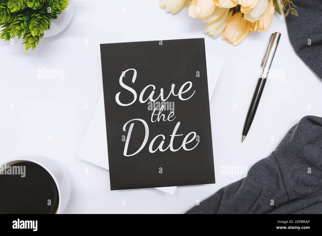 Overhead view of black invitation card on white desk. Save the Date. Stock Photo