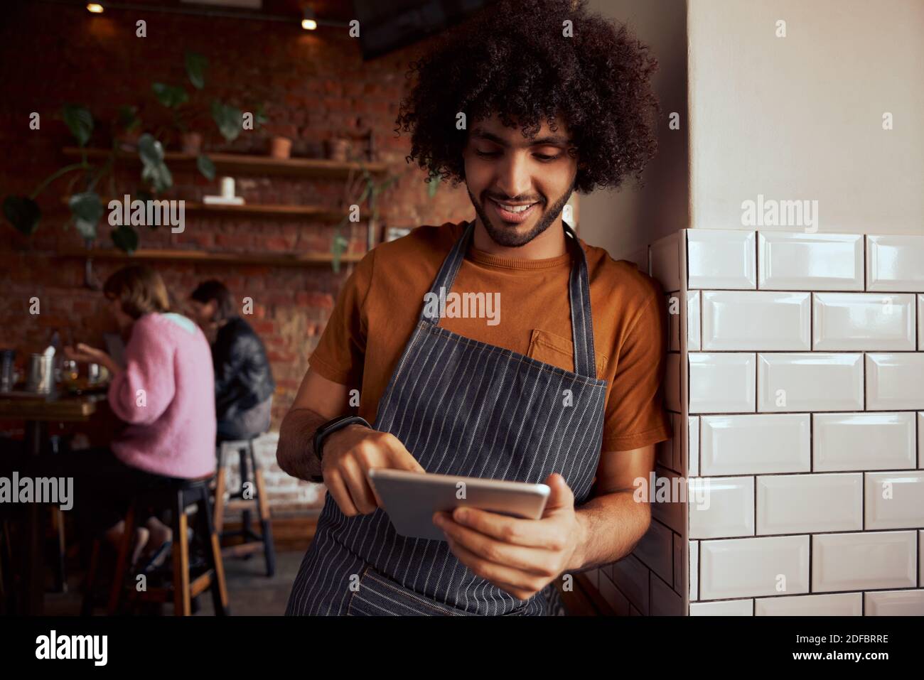 Young male waiter standing at restaurant leaning on wall using digital tablet Stock Photo