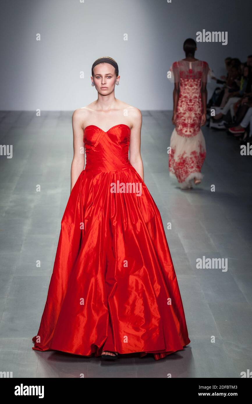 Model walking down runway in red evening gown models on catwalk at London Fashion Weekend show, 2014 Stock Photo
