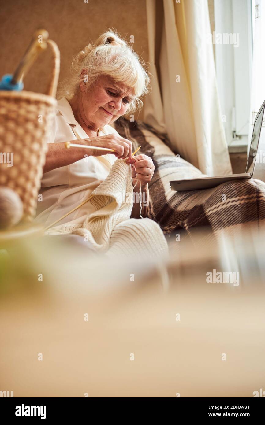 Nice old woman knitting and using notebook at home Stock Photo
