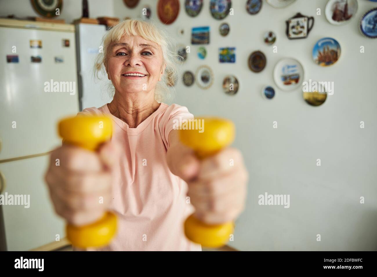 Joyful senior woman doing exercise with dumbbells at home Stock Photo